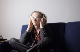 Junger Mann entspannt zu Hause auf dem Sofa und hört Musik über Over-Ear-Kopfhörer