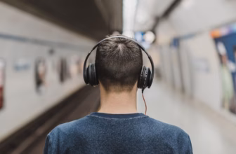Mann mit Over-Ear-Kopfhörern wartet an einem Bahngleis
